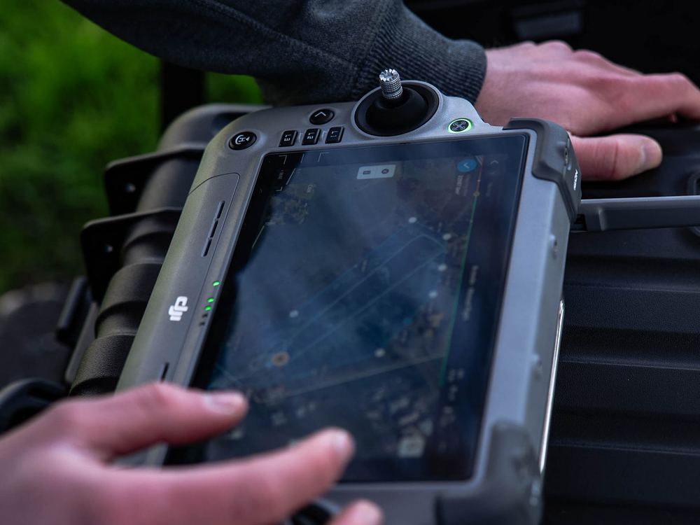 Hands on a drone controller showing a mapping flight plan